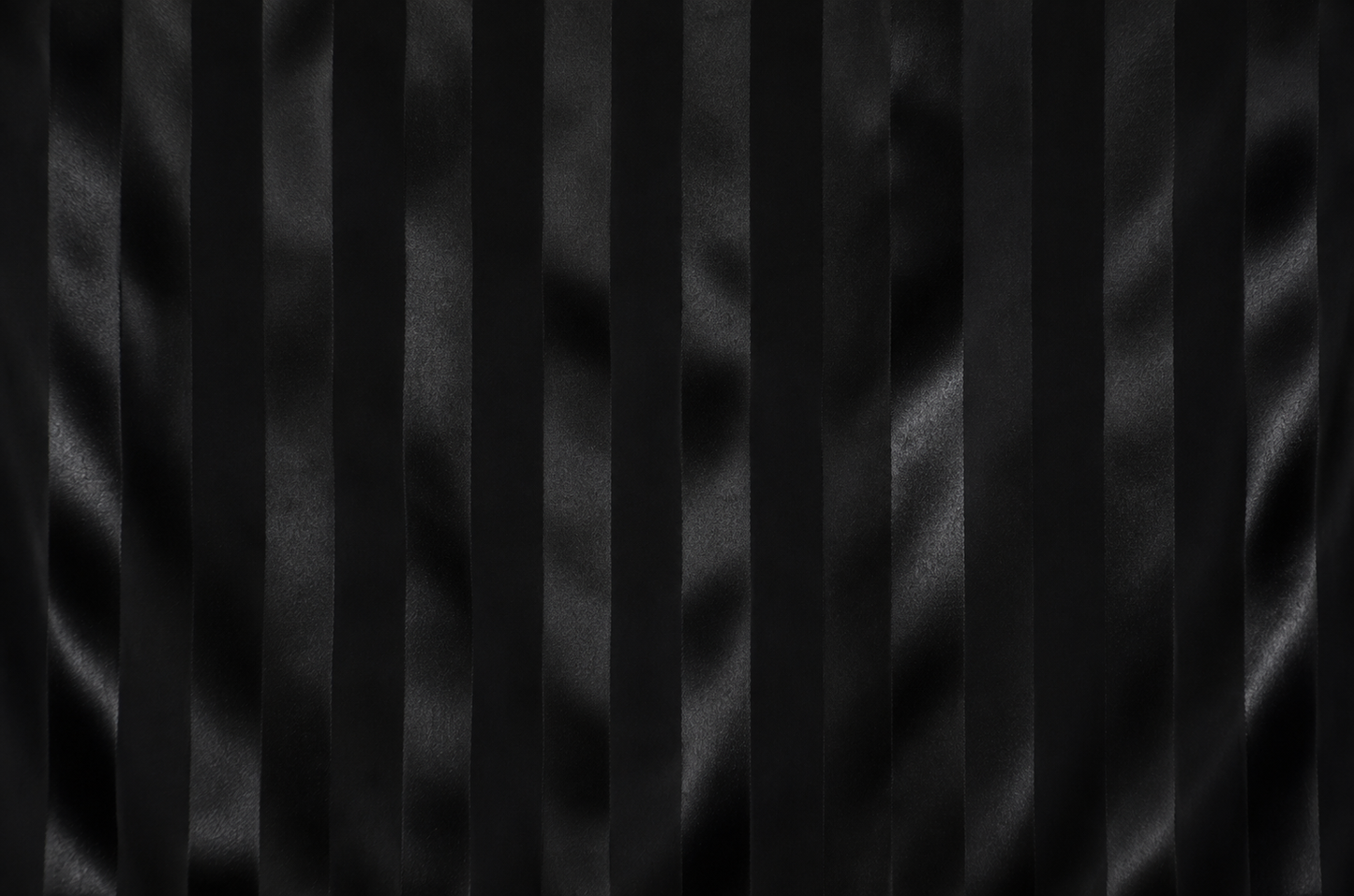 Black pleated fabric texture with vertical satin-like folds and a subtle sheen.