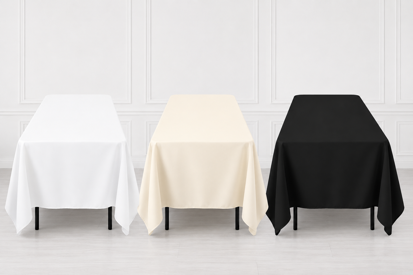 Three rectangular tablecloths in white, cream, and black are draped over matching tables against a light gray paneled wall and floor.