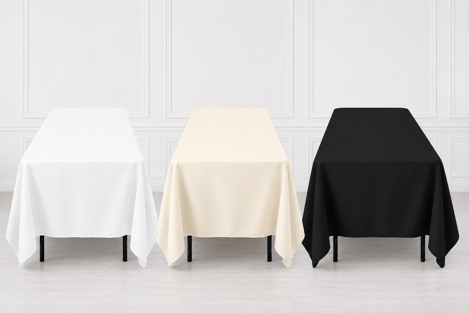 Three rectangular tablecloths in white, cream, and black are draped over matching tables against a light gray paneled wall and floor.