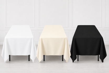 Three rectangular tablecloths in white, cream, and black are draped over matching tables against a light gray paneled wall and floor.