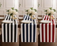 Three striped table runners displayed on a dining table with white plates, gold cutlery, and white flower arrangements. The left runner is black and white, the middle is navy and white, and the right is red and white.