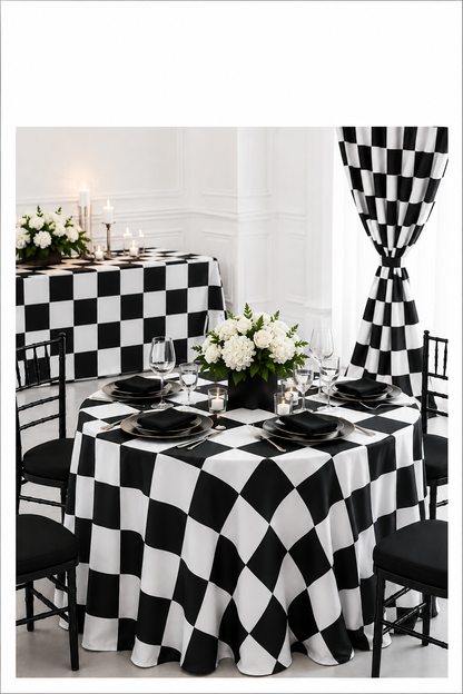 A black and white checkered tablecloth draped over a round dining table, styled with black plates, white floral centerpieces, and black chairs. A matching checkered curtain hangs in the background against a white paneled wall.