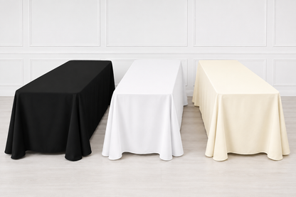 Three rectangular table covers in black, white, and cream are draped over matching tables in a bright studio setting with a white paneled wall and light wood floor.