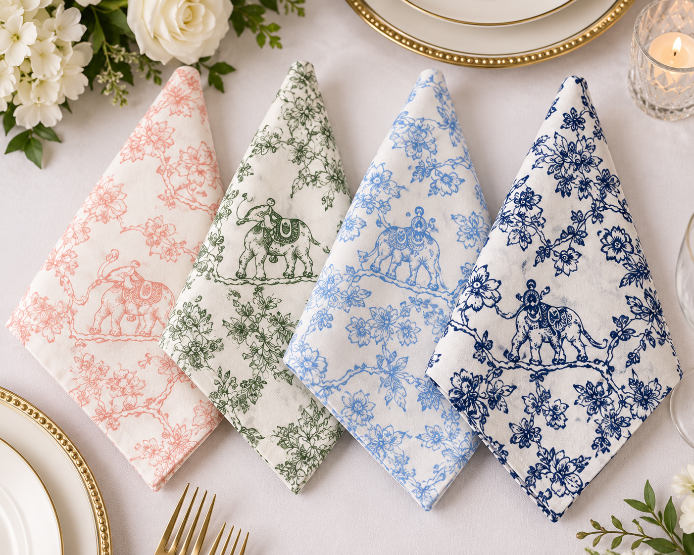 Four folded cloth napkins with classic toile patterns are arranged on a white tablecloth. The napkins feature different colorways: pink, sage green, light blue, and navy blue.