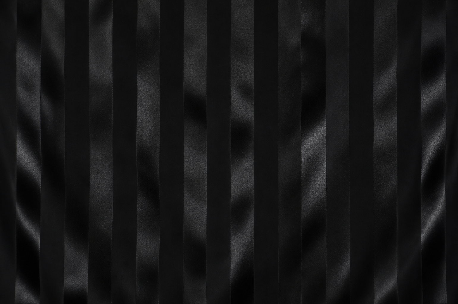 Black pleated fabric texture with vertical satin-like folds and a subtle sheen.
