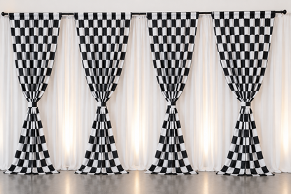 Five black and white checkered curtains tied at the bottom, hanging in front of sheer white drapes on a rod, with a reflective dark floor below.