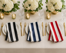 Three place settings on a cream tablecloth, each with a white plate, gold-toned cutlery, a striped napkin, and floral centerpieces with gold candle holders.